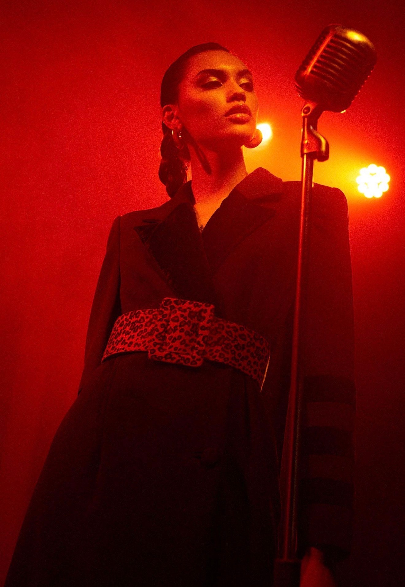 Artist performing beside a vintage microphone under red stage lighting