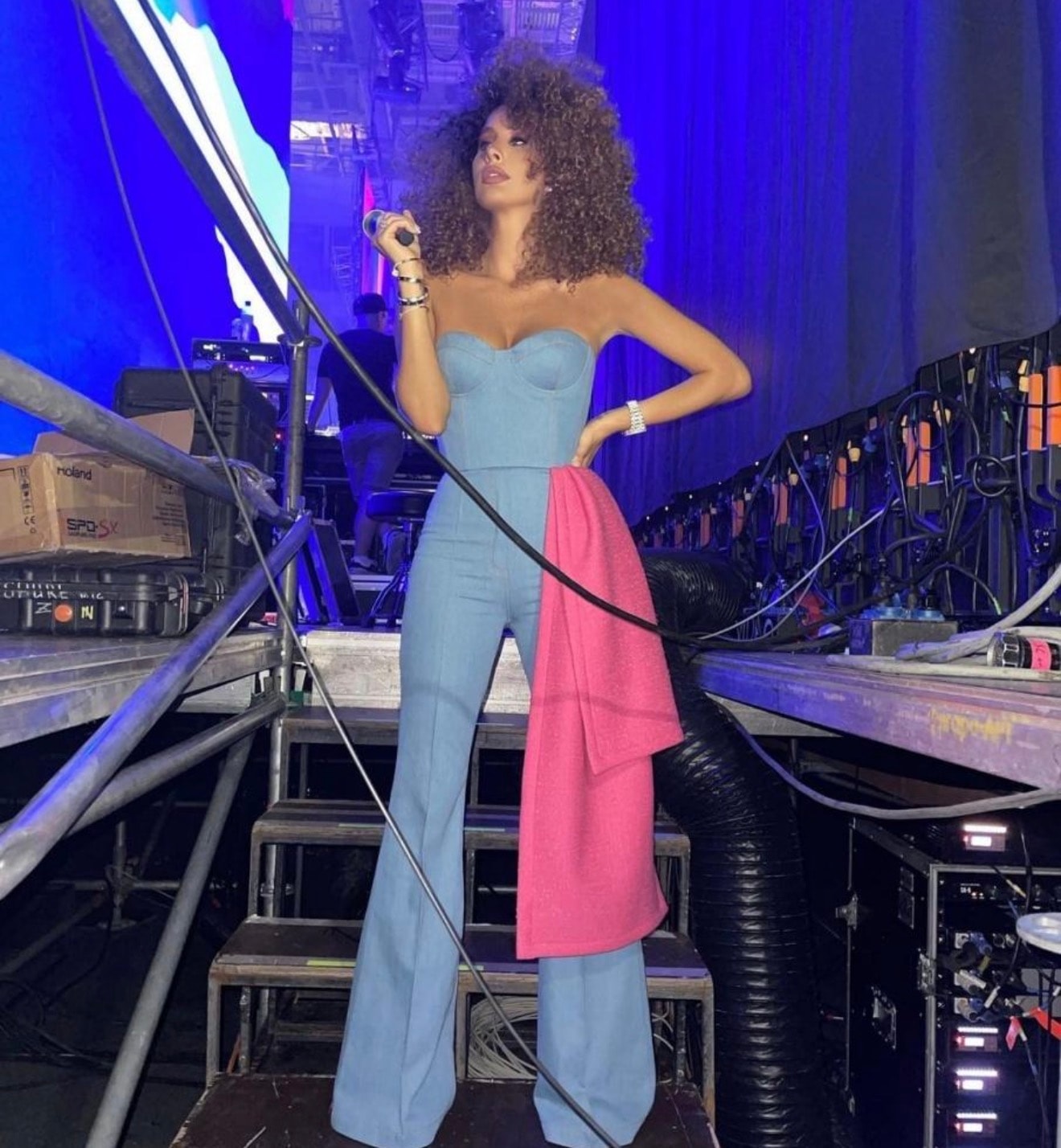 Artist in a blue outfit backstage beside stage equipment